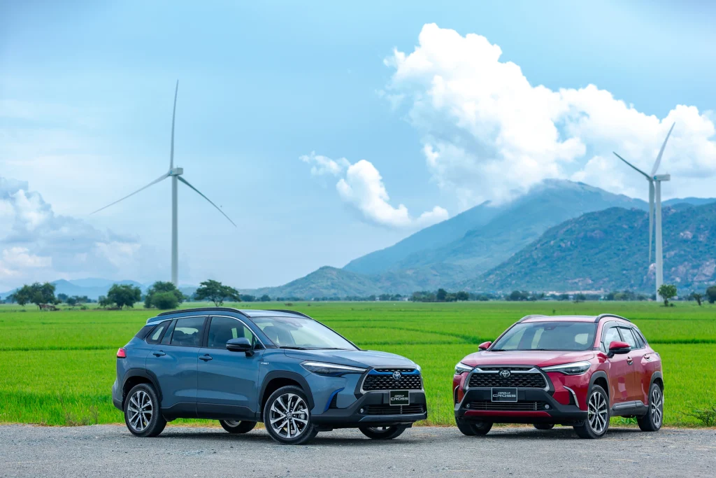 xe Corolla Cross 2024 màu xanh xám và màu đỏ bên cạnh cánh đồng